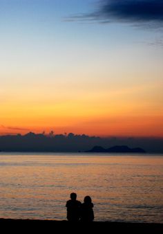 two people sitting on the beach watching the sunset