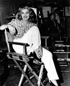 a woman sitting on top of a wooden chair in a room with other people around