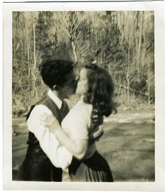 an old black and white photo of two people kissing each other in front of trees