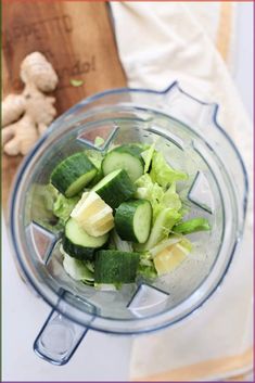 cucumber and lemon slices in a blender on a table next to a cutting board