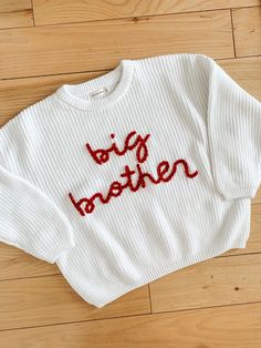 a white sweater with the words big brother embroidered on it sitting on a wooden floor