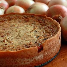 a pie sitting on top of a wooden table next to some onions and an apple