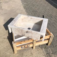 a white sink sitting on top of a wooden pallet next to a brick sidewalk