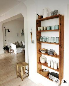 a wooden shelf filled with dishes on top of a hard wood floor next to a white wall