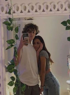 a man and woman taking a selfie in front of a mirror with ivy growing on it