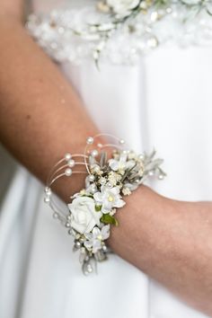 a woman in a white dress is wearing a bracelet with flowers and pearls on it