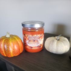 two pumpkins sitting on a table next to a jar of orange marmalade