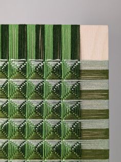 the green and white weaving is being displayed in front of a gray background with small squares on it