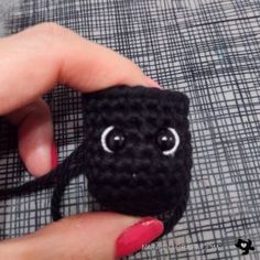 a hand holding a small black crocheted object with eyes on it's face