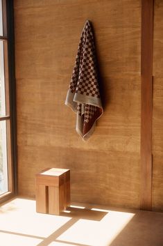 a towel hanging on the side of a wooden wall next to a stool and window