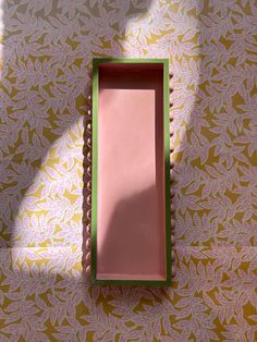 an empty pink box sitting on top of a floral wallpapered floor with green trim