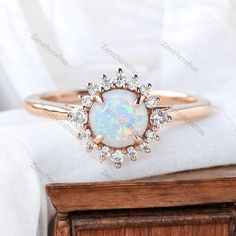 an opal and diamond ring sits on top of a white cloth next to a wooden box