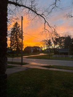 the sun is setting over an empty street in front of some houses and trees with no leaves on them