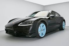 a black sports car with blue rims parked in a white room next to a wall