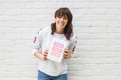 a woman standing in front of a white brick wall holding up a pink sign that says,