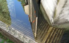 the reflection of an old wooden bridge in water with grass and trees on it's sides