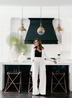 a woman standing in front of a kitchen counter with lights hanging from it's ceiling