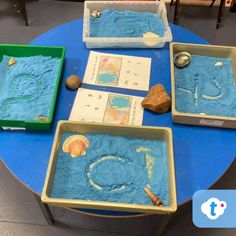 three trays filled with blue sand and seashells on top of a table