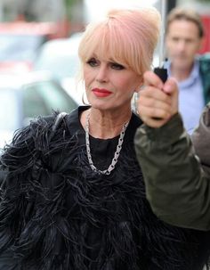 a woman with blonde hair holding an umbrella and pointing at the camera while another man looks on