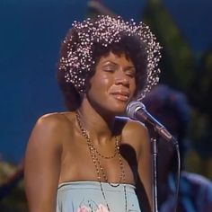 a woman wearing a flowered hat and singing into a microphone with her eyes closed