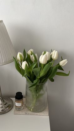 white tulips in a glass vase on a table next to a small lamp