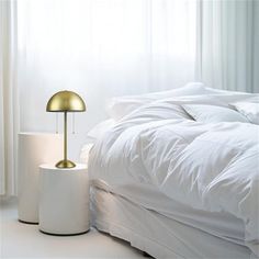 a white bed sitting next to a lamp on top of a table