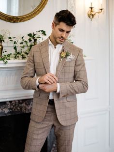 a man in a tan suit and flower boutonniere standing next to a fireplace