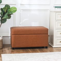 a brown leather storage box sitting on top of a wooden floor next to a plant