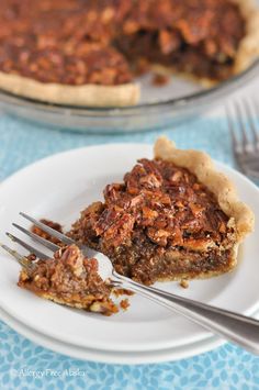 a slice of pecan pie on a white plate with a fork and another pie in the background