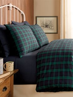 a bed with blue and green plaid comforter on it next to a wooden headboard