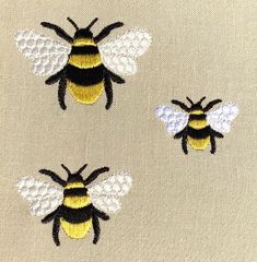 three embroidered bees sitting next to each other on a piece of white fabric with black and yellow details