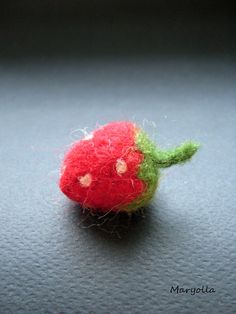 a needle - felted red and green object sitting on top of a black surface