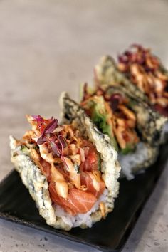 two sushi rolls on a black plate with toppings and garnishes