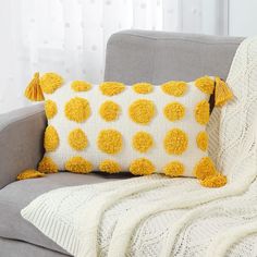 a gray couch with a white and yellow throw pillow on it's back next to a window