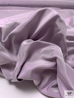 an unmade bed with purple sheets on top of it and a white pillow in the background