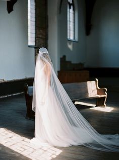 a woman in a wedding dress and veil is sitting on a bench with her back to the camera