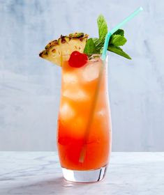 a drink with pineapple and mint garnish in a tall glass on a marble table