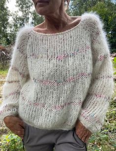 an older woman standing in the grass wearing a white sweater with pink and blue stripes