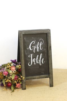 a chalkboard sign with the words gift table written on it next to a bouquet of flowers