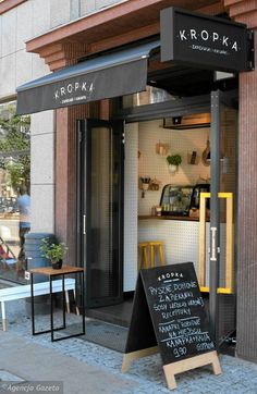 a small store front with a menu board in the doorway and two tables on the sidewalk next to it