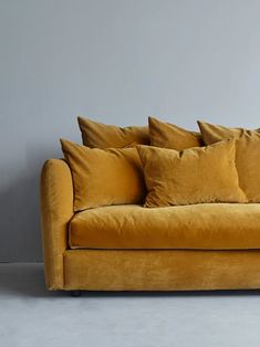 a yellow couch with four pillows on it's back and one arm resting against the wall