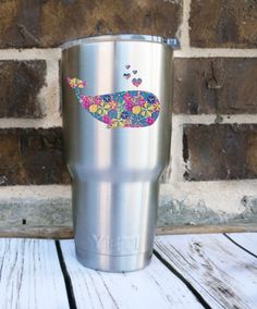 a stainless steel tumbler with a colorful whale design on the side, sitting against a brick wall