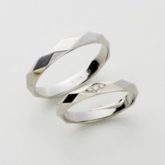 two white gold wedding rings with diamonds on each side, set against a plain background