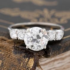 an old - fashioned diamond engagement ring sits on top of a piece of wood in front of a book