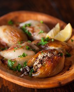 a wooden bowl filled with food on top of a wooden table next to lemon wedges