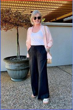 an older woman standing in front of a potted plant wearing sunglasses and a pink cardigan