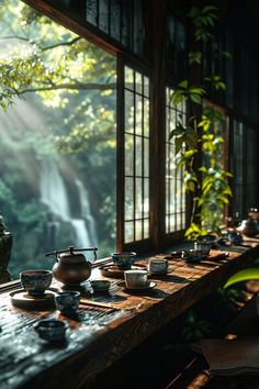 a long table with tea cups on it in front of a window overlooking a waterfall