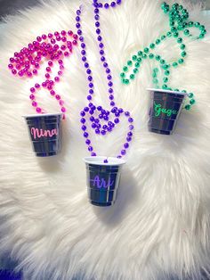 three cups with beaded necklaces on them sitting on a white fur covered surface