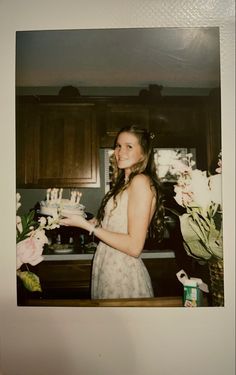 a woman standing in front of a kitchen counter holding a cake with candles on it