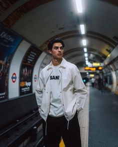 a man standing in front of a subway station with his hands in his pockets and looking at the camera